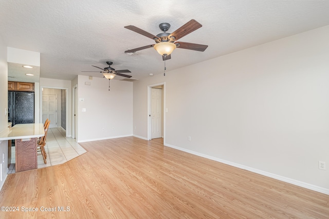 unfurnished room featuring a textured ceiling, light wood-type flooring, and ceiling fan