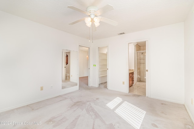 unfurnished bedroom with connected bathroom, a walk in closet, a closet, ceiling fan, and light carpet