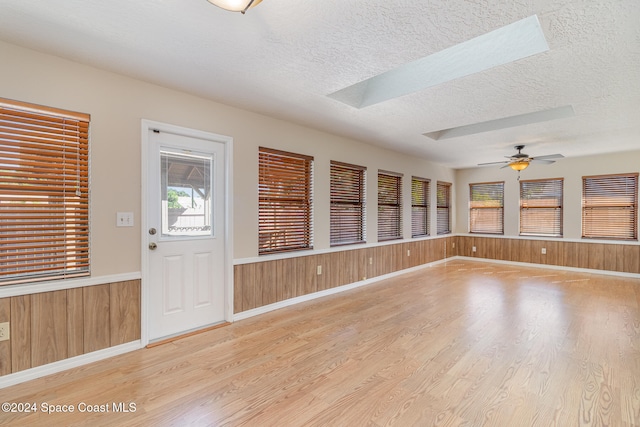 interior space featuring a skylight, ceiling fan, wood-type flooring, a textured ceiling, and wooden walls