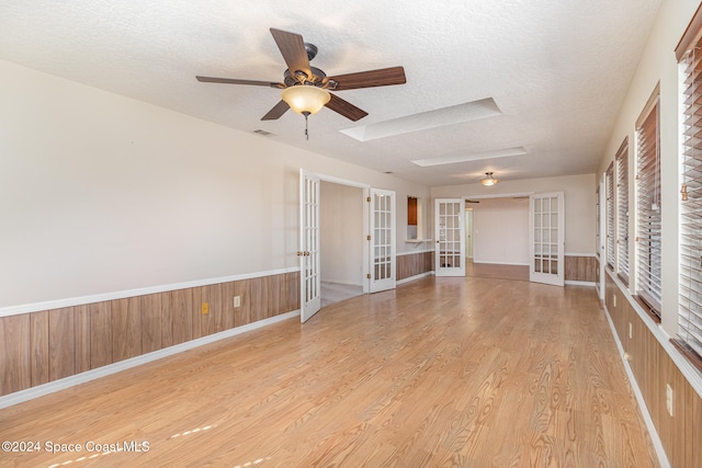 unfurnished living room featuring a textured ceiling, ceiling fan, light hardwood / wood-style floors, and french doors