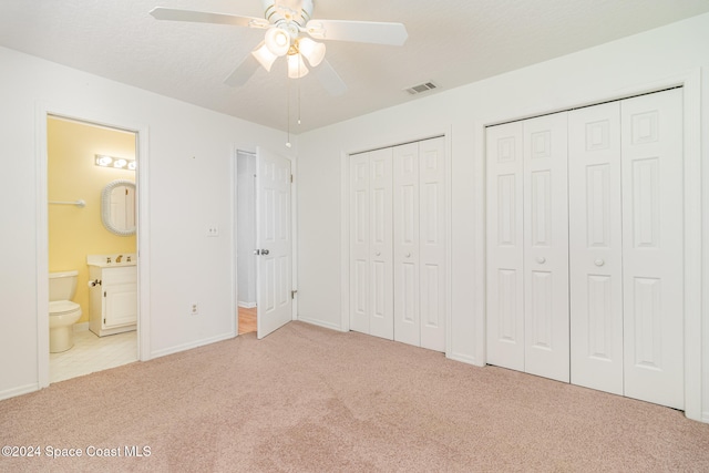 unfurnished bedroom with connected bathroom, light colored carpet, ceiling fan, and multiple closets