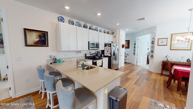 kitchen featuring sink, light hardwood / wood-style flooring, decorative light fixtures, kitchen peninsula, and stainless steel appliances