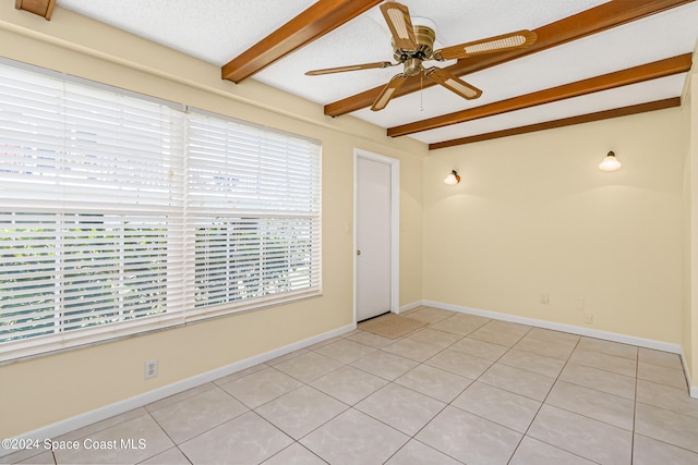 empty room with beamed ceiling, ceiling fan, light tile patterned floors, and a textured ceiling