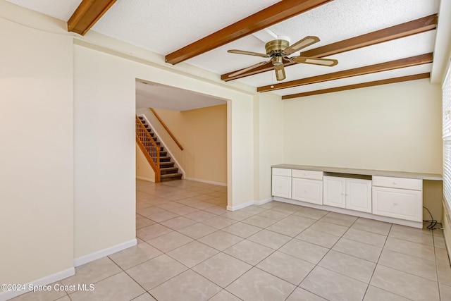 unfurnished room featuring beam ceiling, ceiling fan, a textured ceiling, light tile patterned floors, and built in desk