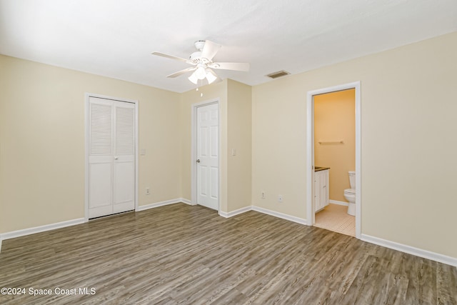 unfurnished bedroom featuring wood-type flooring, a closet, ensuite bath, and ceiling fan