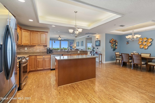 kitchen with appliances with stainless steel finishes, a raised ceiling, and pendant lighting