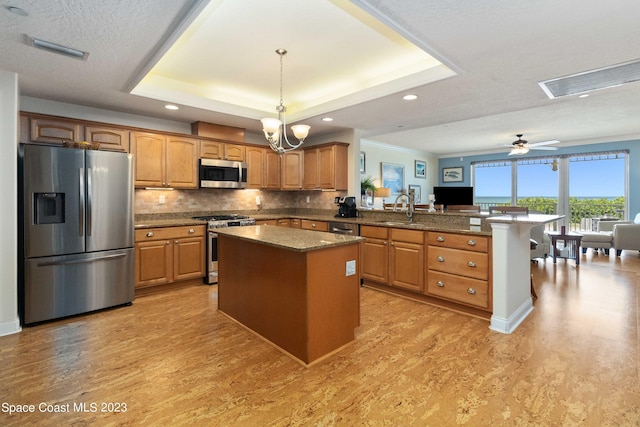 kitchen with sink, stainless steel appliances, a tray ceiling, decorative backsplash, and a kitchen island