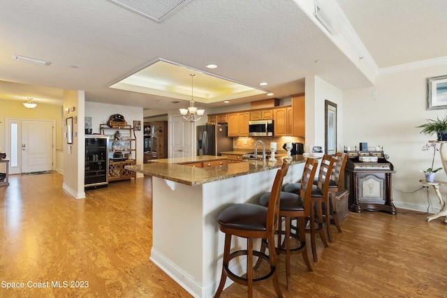 kitchen featuring appliances with stainless steel finishes, light wood-type flooring, a kitchen breakfast bar, a textured ceiling, and dark stone countertops