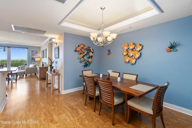 dining area with a tray ceiling, wood-type flooring, a notable chandelier, and ornamental molding