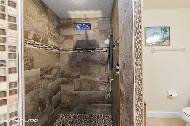 bathroom with tile patterned flooring, toilet, a textured ceiling, and a tile shower