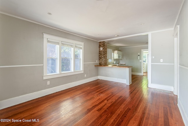 unfurnished living room featuring washer / dryer, crown molding, dark wood-type flooring, and sink