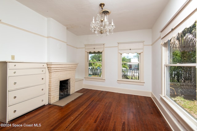 unfurnished living room featuring a chandelier, a brick fireplace, and dark wood-type flooring