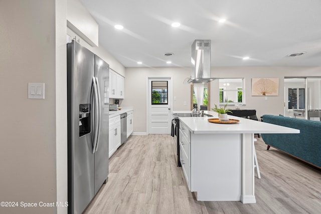 kitchen featuring white cabinets, appliances with stainless steel finishes, island range hood, and a center island with sink