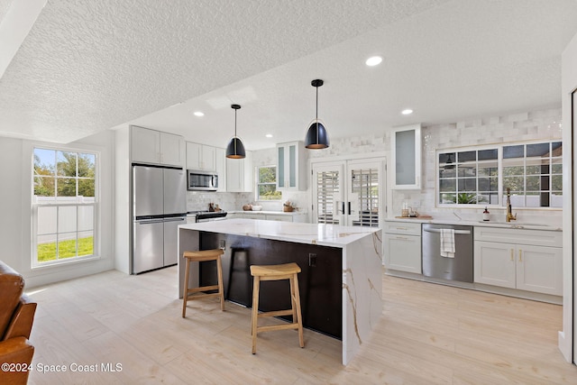 kitchen featuring white cabinets, a textured ceiling, appliances with stainless steel finishes, a kitchen island, and light stone counters