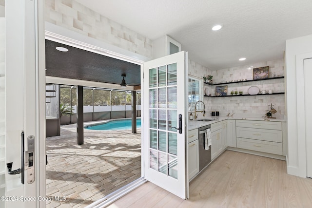 bar featuring sink, stainless steel dishwasher, decorative backsplash, light hardwood / wood-style floors, and white cabinetry