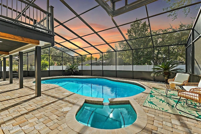 pool at dusk with a lanai, an in ground hot tub, and a patio