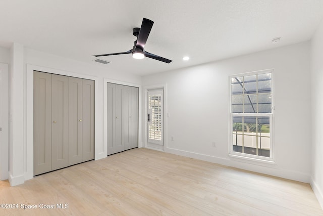 unfurnished bedroom featuring ceiling fan, two closets, and light wood-type flooring