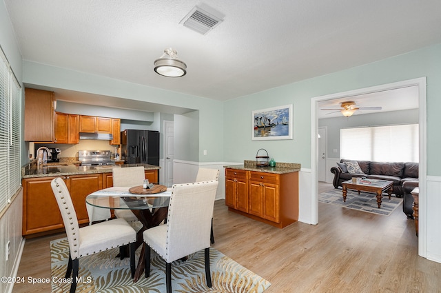 dining room featuring ceiling fan, sink, a textured ceiling, and light wood-type flooring