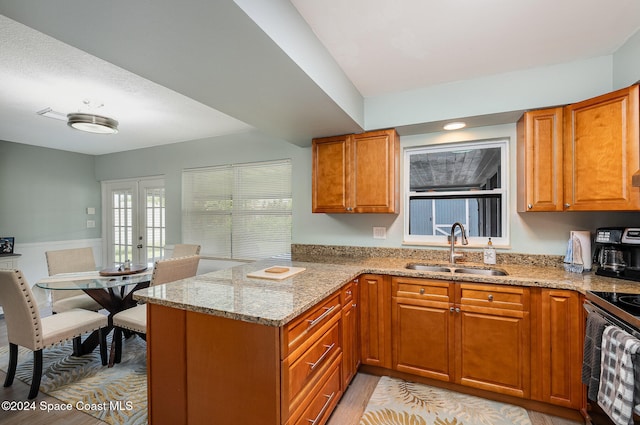 kitchen with sink, light stone counters, kitchen peninsula, stainless steel range with electric cooktop, and light wood-type flooring