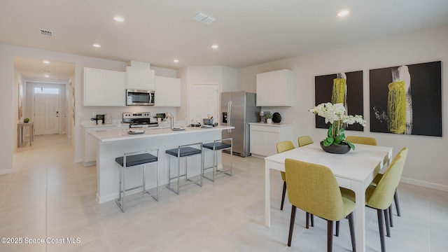 kitchen with visible vents, stainless steel appliances, a center island with sink, and white cabinetry