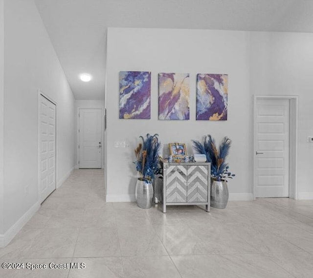 hall featuring light tile patterned floors and lofted ceiling