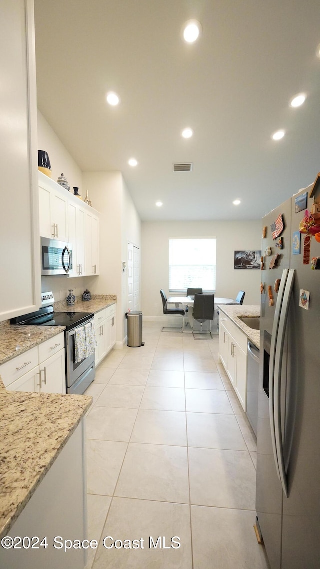 kitchen with white cabinets, appliances with stainless steel finishes, light stone counters, and light tile patterned flooring