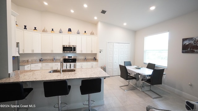 kitchen featuring white cabinetry, sink, light stone countertops, vaulted ceiling, and appliances with stainless steel finishes