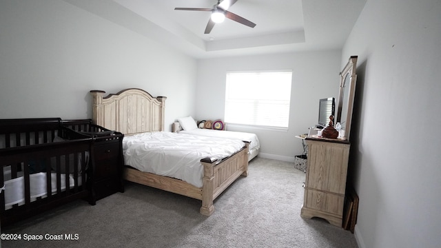 carpeted bedroom featuring a raised ceiling and ceiling fan