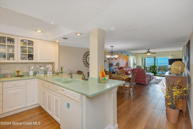 kitchen featuring light countertops, glass insert cabinets, a sink, dishwasher, and a peninsula