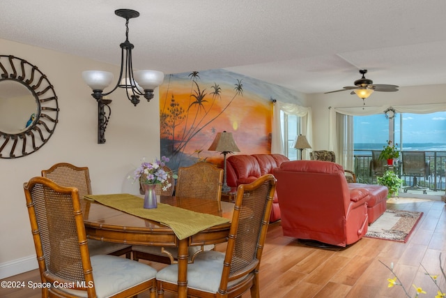 dining room with a textured ceiling, ceiling fan with notable chandelier, a water view, and wood finished floors