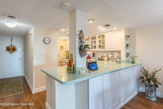 kitchen with a peninsula, visible vents, white cabinetry, light countertops, and glass insert cabinets