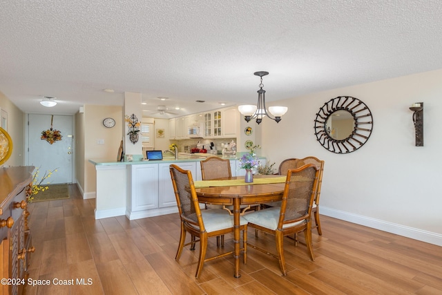 dining space featuring light wood-type flooring, a textured ceiling, baseboards, and an inviting chandelier