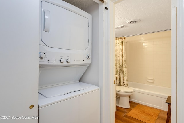 clothes washing area featuring stacked washer and dryer, visible vents, a textured ceiling, and wood finished floors