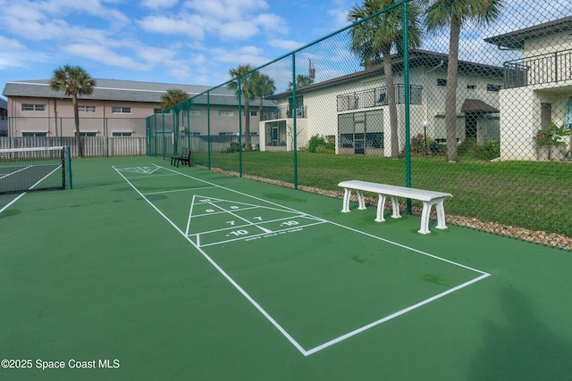 surrounding community with a tennis court, shuffleboard, fence, and a lawn