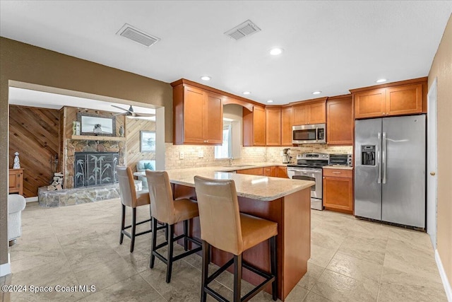 kitchen featuring light stone countertops, a kitchen breakfast bar, stainless steel appliances, a fireplace, and wood walls