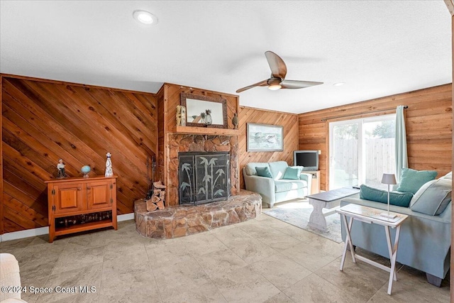 living room featuring a fireplace, ceiling fan, and wooden walls