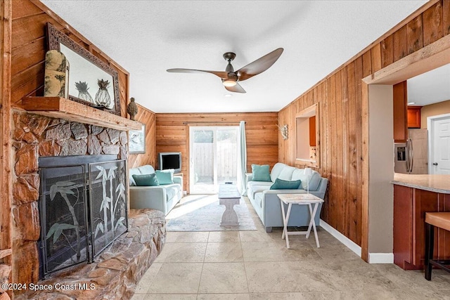 living room with a stone fireplace, ceiling fan, wooden walls, and a textured ceiling