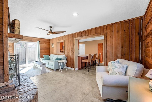 living room featuring a textured ceiling, ceiling fan, and wood walls