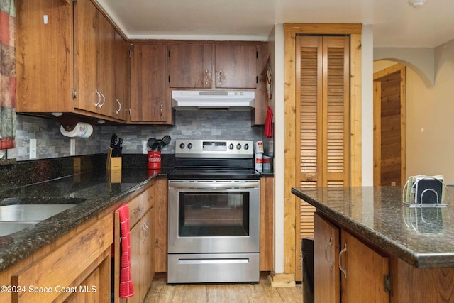 kitchen with stainless steel electric range, decorative backsplash, light wood-type flooring, and dark stone counters