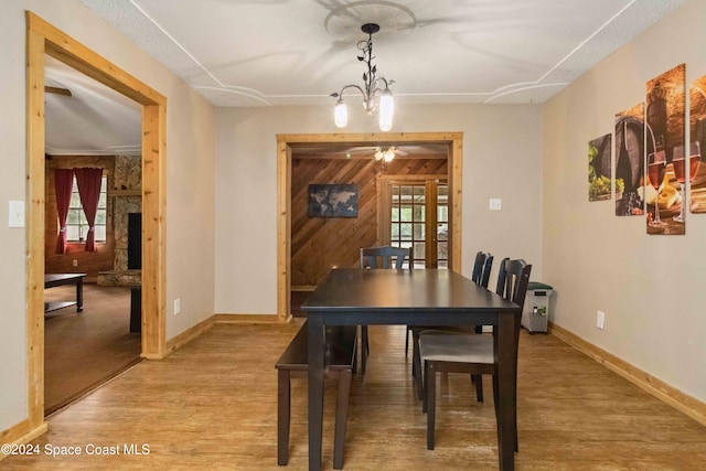 dining room with wooden walls, light hardwood / wood-style flooring, and ceiling fan with notable chandelier