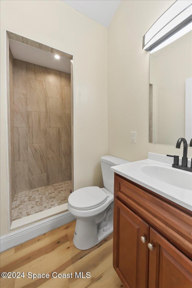 bathroom featuring a tile shower, toilet, vanity, and hardwood / wood-style flooring