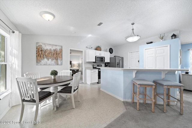 kitchen with stainless steel appliances, pendant lighting, a breakfast bar area, white cabinetry, and lofted ceiling