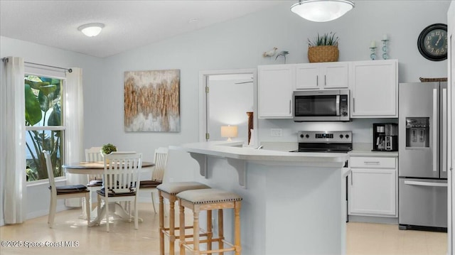 kitchen featuring lofted ceiling, white cabinetry, stainless steel appliances, and a breakfast bar