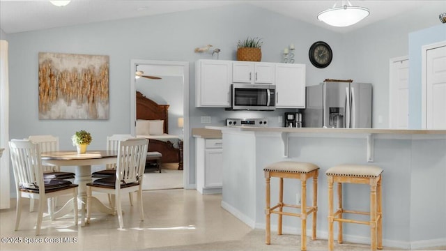 kitchen featuring appliances with stainless steel finishes, a kitchen breakfast bar, ceiling fan, white cabinets, and lofted ceiling