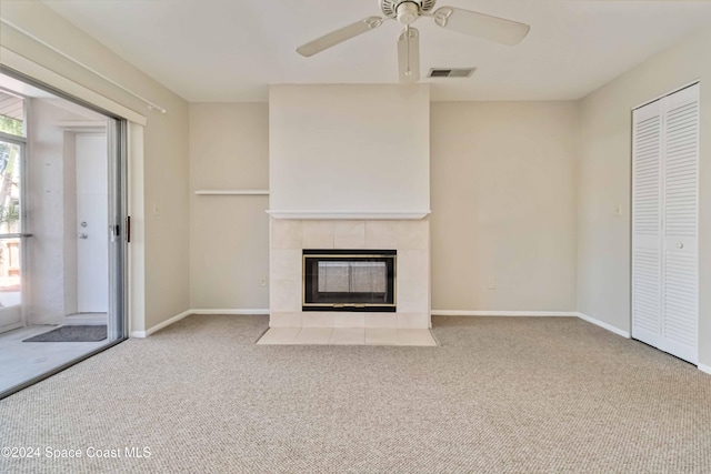 unfurnished living room featuring a tiled fireplace, ceiling fan, and carpet floors