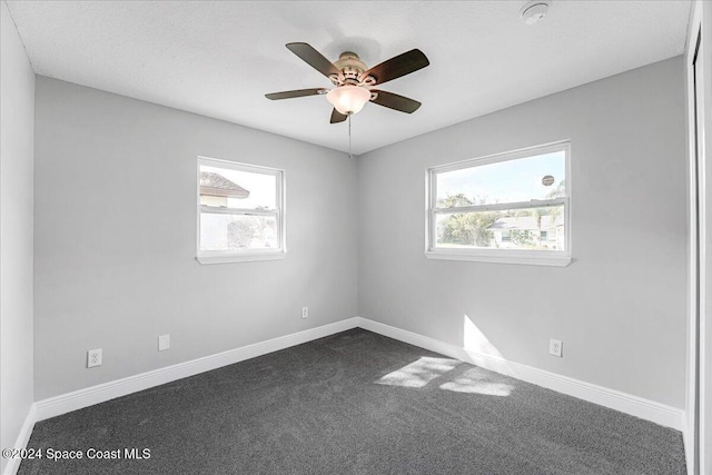 empty room with plenty of natural light, dark carpet, and ceiling fan