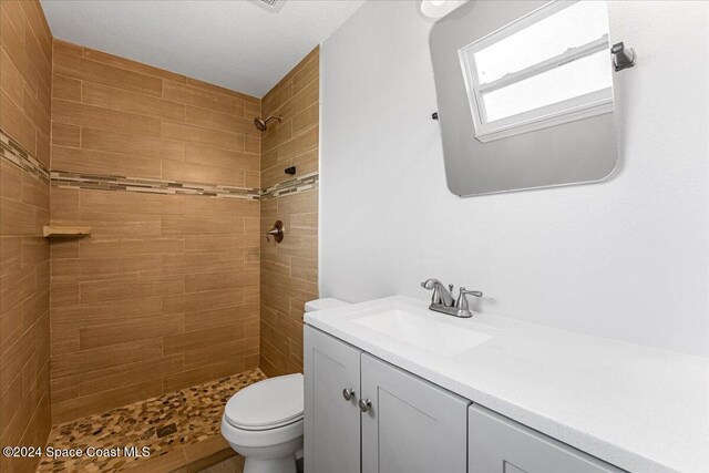 bathroom with a tile shower, vanity, a textured ceiling, and toilet