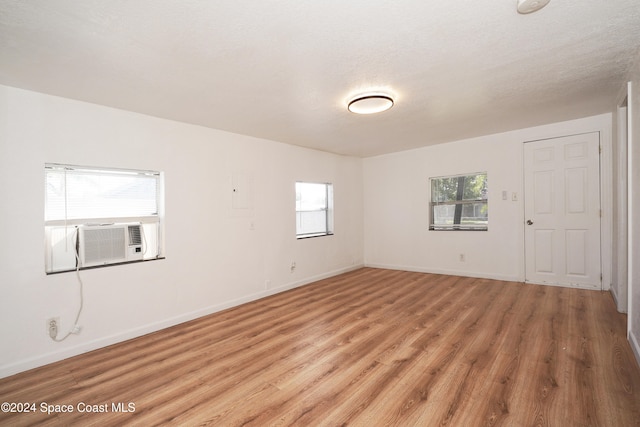 spare room with a textured ceiling, light wood-type flooring, plenty of natural light, and cooling unit