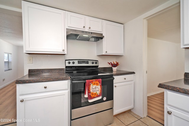 kitchen featuring stainless steel electric range oven, light hardwood / wood-style flooring, white cabinets, and dark stone counters