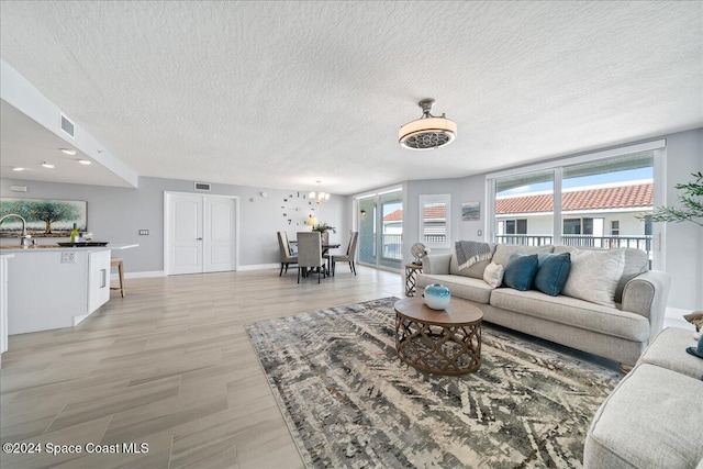 living room with a chandelier, a textured ceiling, light wood-type flooring, and sink